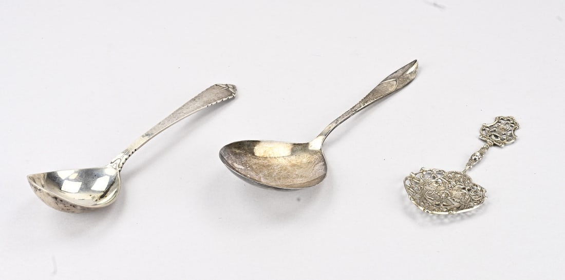 3 parts silver: Three pieces of silver cutlery, 833/000, with an openwork petit four server, MT.: unclear Amsterdam, year:M:1922, 14 cm. And 2 Art Deco serving spoons, a serving spoon with a hammered semi-circular