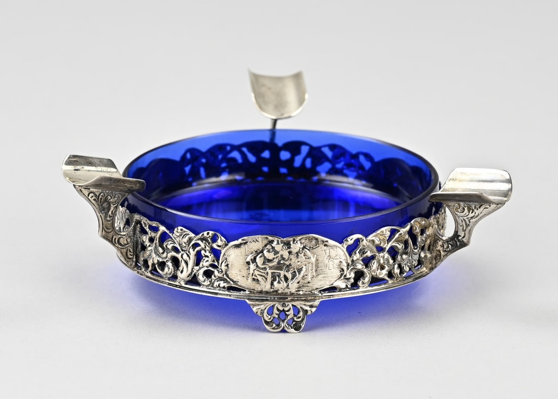 Silver ashtray with blue glass: Silver ashtray, 833/000, with blue glass inner bowl. Silver openwork round holder featuring floral decoration and 3 medallions with motifs. Silver approx. 49 grams. 11x11x3cm. Maker: Firma Dahlia,