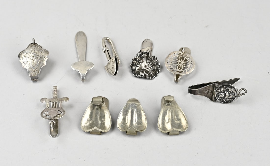 Lot of small skirt hooks, 10x: Lot of 10 small skirt hooks, of which 7 are silver, 833/000, various contoured models, and 3 white metal models. Silver approx. 80 grams. 5-7cm. In reasonably good condition.