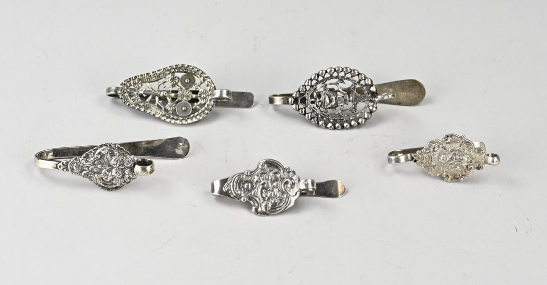 Lot of silver skirt hooks, 5x: Lot of five silver skirt hooks, 833/000, contoured models, partly decorated with figures and floral motifs. 2nd century antique models marked AB. Size 7.5-11 cm. Total approx. 210 grams. In good condi