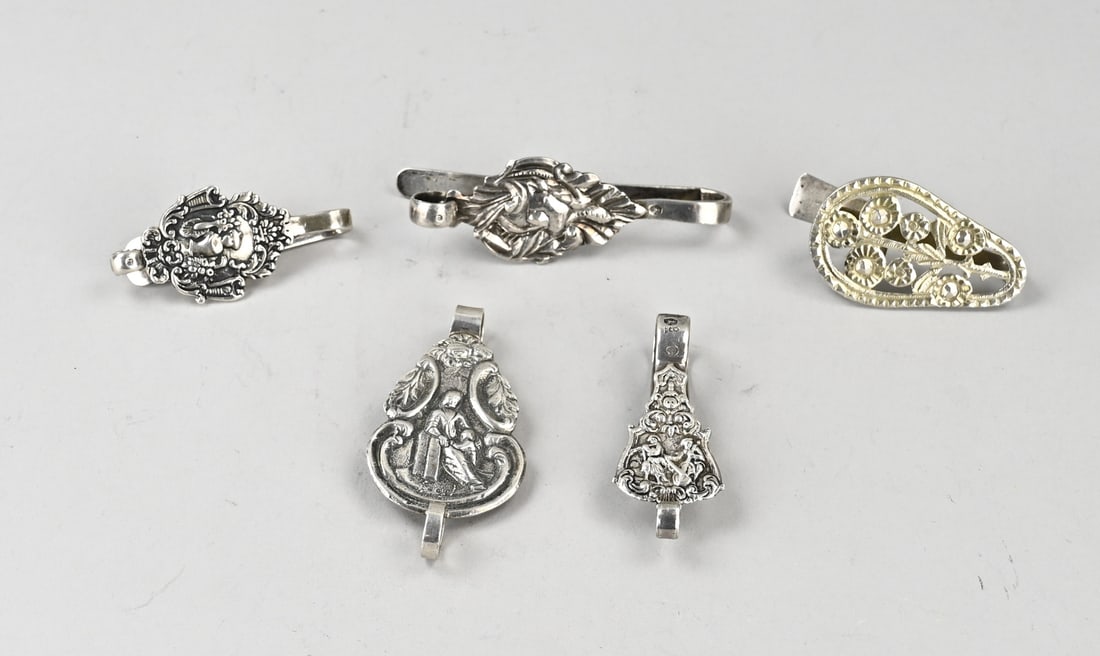 Lot of silver skirt hooks, 5x: Lot of five silver skirt hooks, 833/000, contoured models, partly decorated with figures and floral motifs. Maker: among others J. van der Ree, Schoonhoven and van der Meulen, Joure. 7.5 x 10 cm. Tota