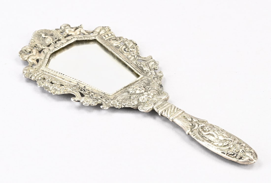 Silver mirror: Small silver hand mirror, hexagonal contoured model with an openwork rim decorated with a peacock, putti, and floral borders. Fitted with a handle featuring a figure and acanthus leaves. Hallmarks