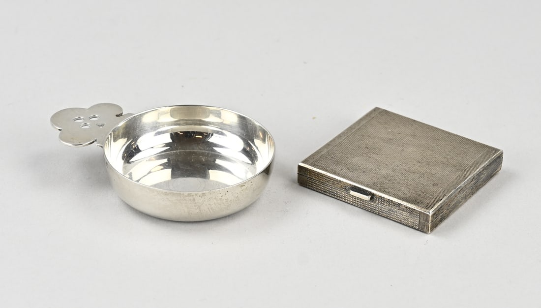 2 parts silver: Two pieces of silver with a French tastevin, 950/000, with a clover-shaped handle. MT.: Tetard, Freres, Paris, after 1903. 9x6.5x2cm. And an English square powder box, 925/000, with guilloche