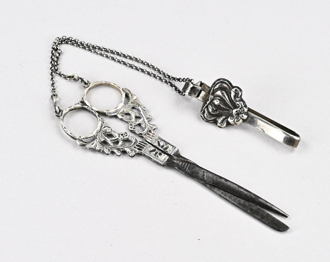 Scissors with silver and skirt hook: Antique scissors with silver handles, chain, and skirt hook, 833/000. Scissors with handles featuring floral patterns and a jasseron chain with a skirt hook with a soldered-on contoured element. 40
