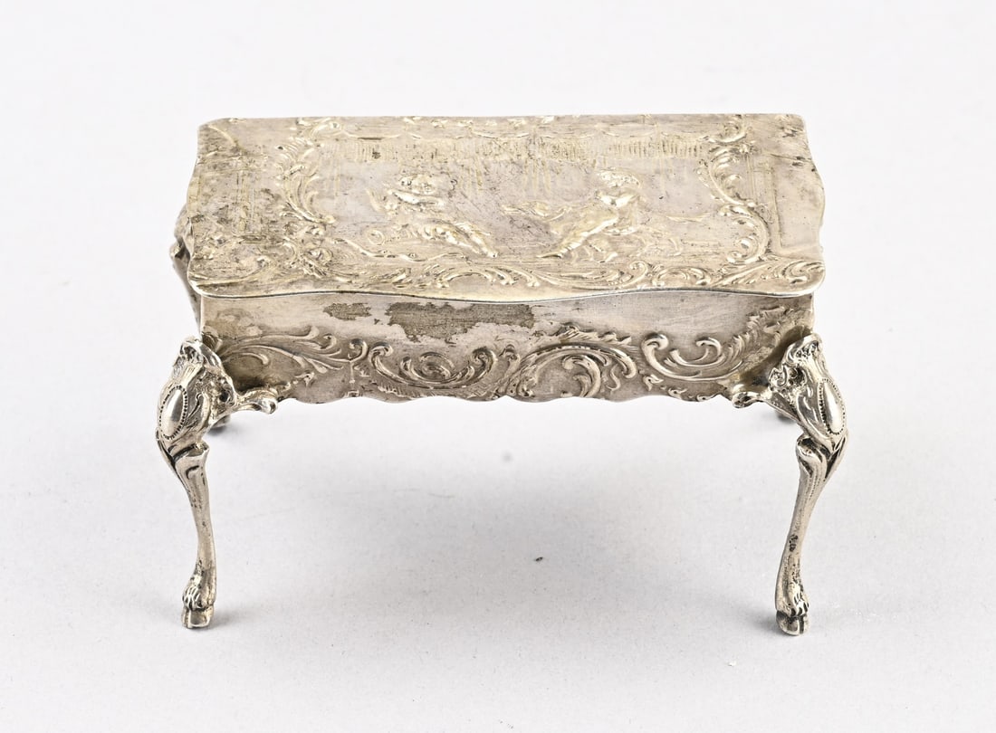 Silver snuff box: Antique silver snuff box in the shape of a table, 800/000. Rectangular table with a contoured top decorated with a depiction of putti, lambrequins, and scrolls. Mounted on 4 claw feet with