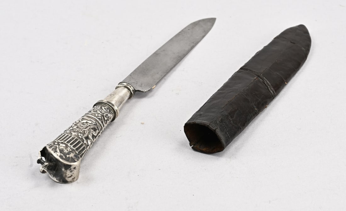 Traveling knife in leather sheath: Antique travel knife in a leather sheath. Travel knife with a silver handle decorated with floral motifs and putti. Crowned with a dog. Middelburg, 1807-1812. 21 cm. In good condition.