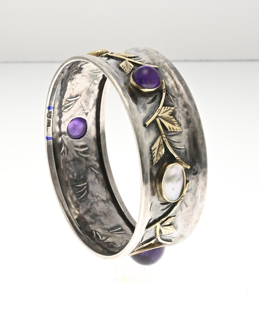Silver bracelet with gold and gemstones: Beautiful wide silver jingle band, 900/000, decorated with gold leaf elements and oval plain settings decorated with amethyst and mother-of-pearl. Marked: 900 rvb. Width 23.5 mm. ø 63 mm. approx.