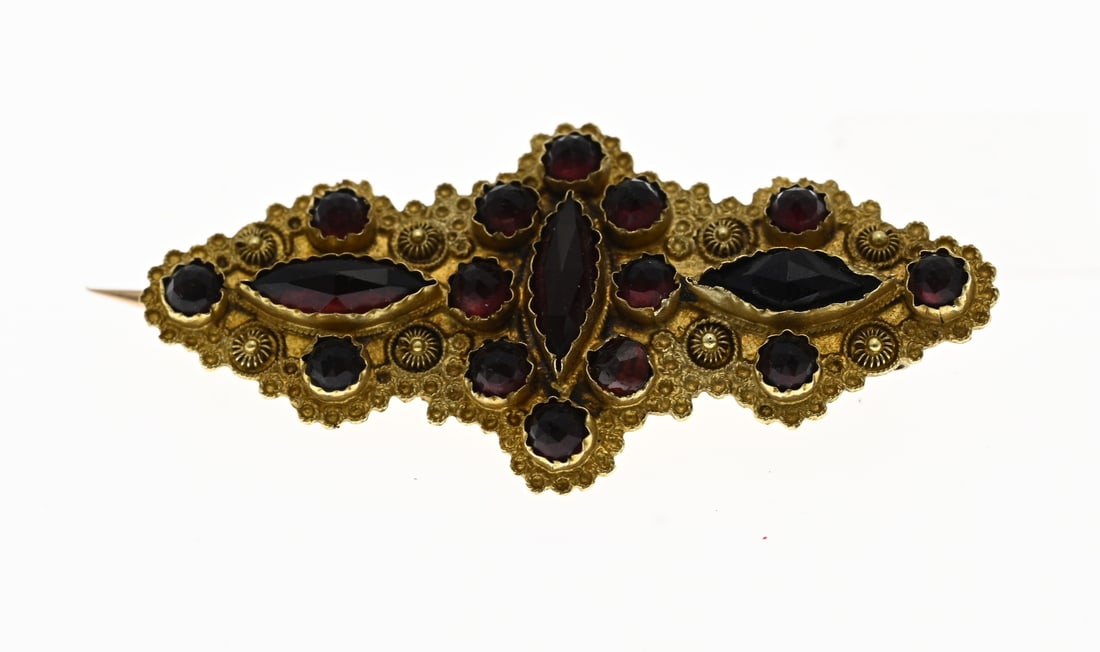 Gold oval rosette brooch with garnet: Yellow gold brooch, 585/000, with garnet. Contoured brooch decorated with twisted ornamentation and buttons. Set with various garnet stones. 17.5x37.5mm. Approx. 3.0 grams. In good condition.