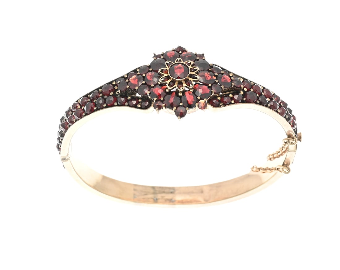 Bangle with grenade: Double bangle with garnet. Hinged bangle fully set with garnet stones and an elaborated section at the top featuring a rosette with garnets. Width 6-22mm. 53x56mm. In good condition.