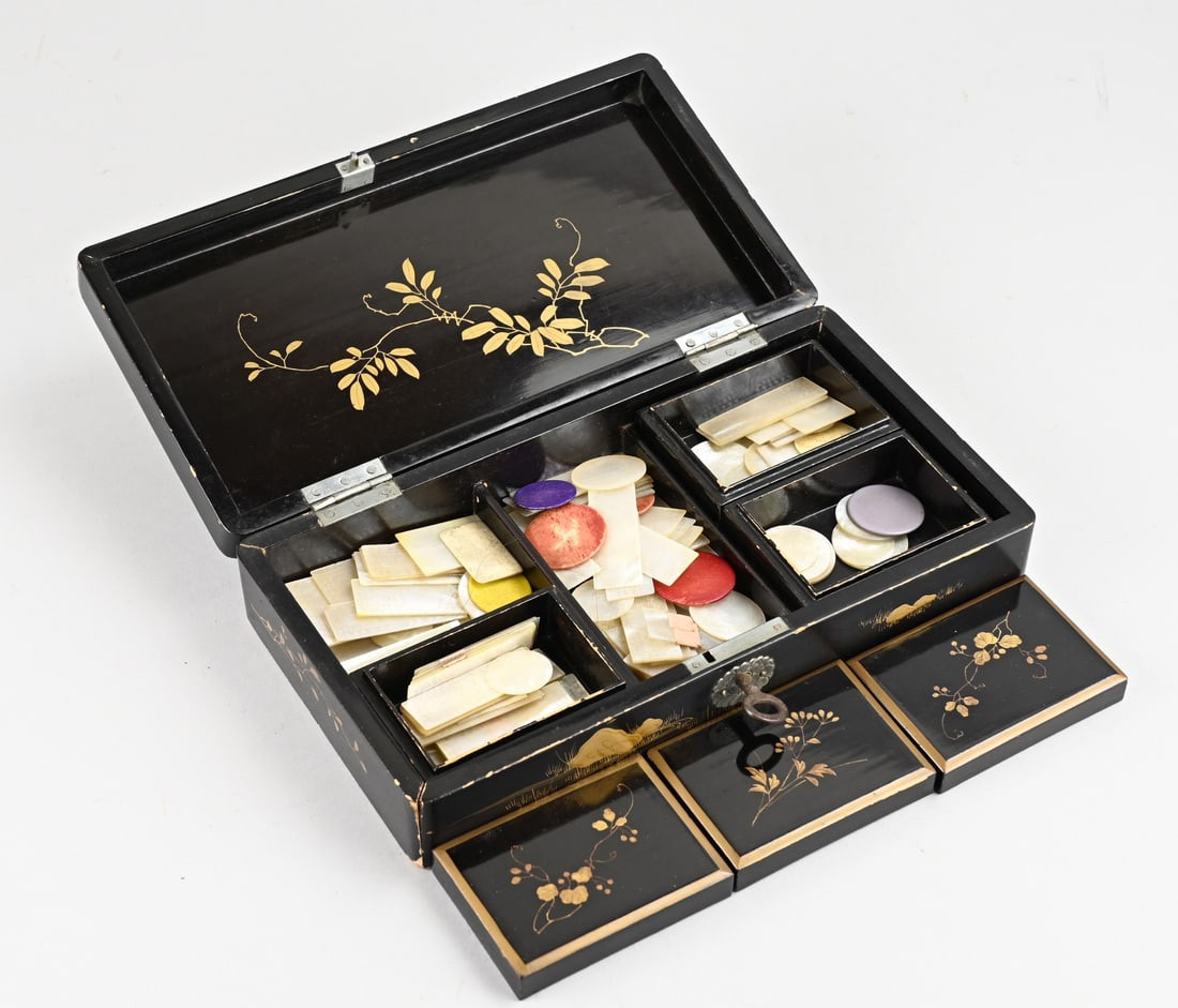 Chinese/Japanese lacquer box with game, 1920: Antique Japanese or Chinese lacquerware game box full of worked mother-of-pearl chips, also featuring figures/floral decoration. Circa 1920. Dimensions: 6 x 27 x 15 cm. In good condition.