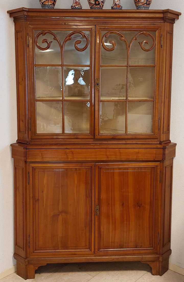 Cherry corner cabinet, 1860: Corner cabinet made of solid cherry wood, with two glazed doors with carvings at the top. A hidden drawer in the middle. Dimensions: H 223 x W 146 cm. In good condition.
