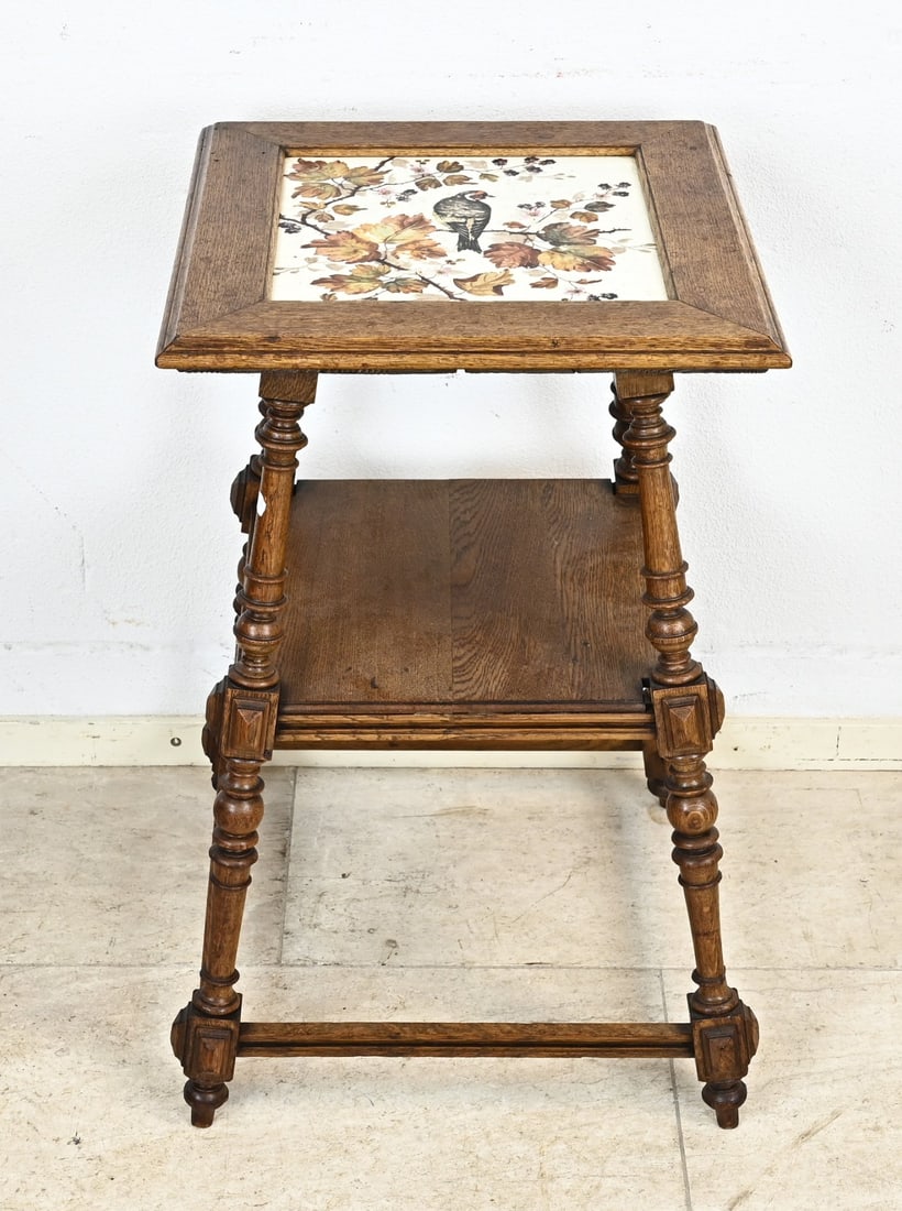 Tiered table, 1890: German Gründerzeit oak etagere table with a ceramic top, decorated with a bird on a grapevine. Circa 1890. Dimensions: 74 x 44 x 44 cm. In good condition.