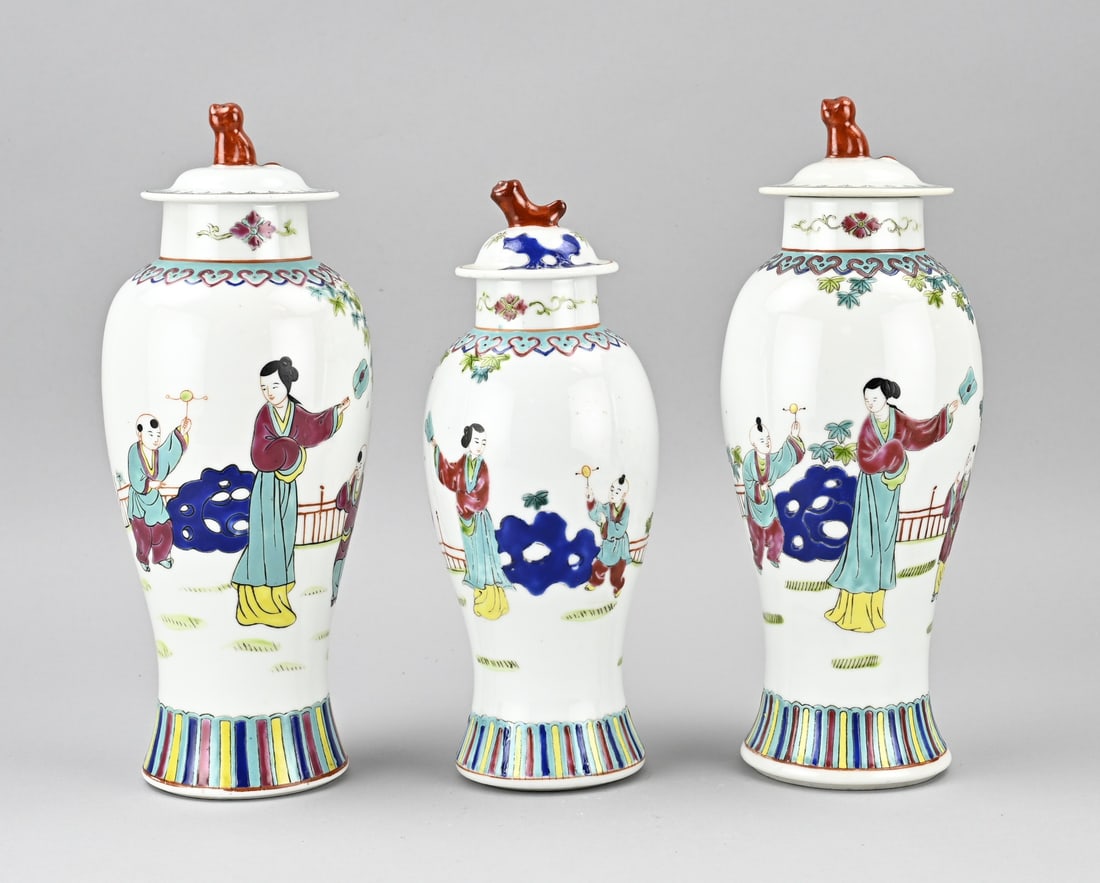 3-Piece Chinese cabinet set, H 28 - 31 cm.: Three-piece Chinese porcelain Rose Family cabinet set/lidded vases. Figures in a garden decor. Base mark. Dimensions: H 28 - 31 cm. In good condition.