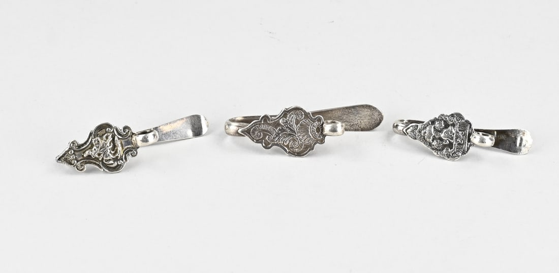 3 Silver skirt hooks, 18th century: Lot of three silver skirt hooks, 18th century, contoured models, some with figures. Masterpiece: D. de Klerk, Haarlem, 1756; J. de Vries, Amsterdam, 1782; A. Kramp, Enkhuizen, 1769. Total approx. 130