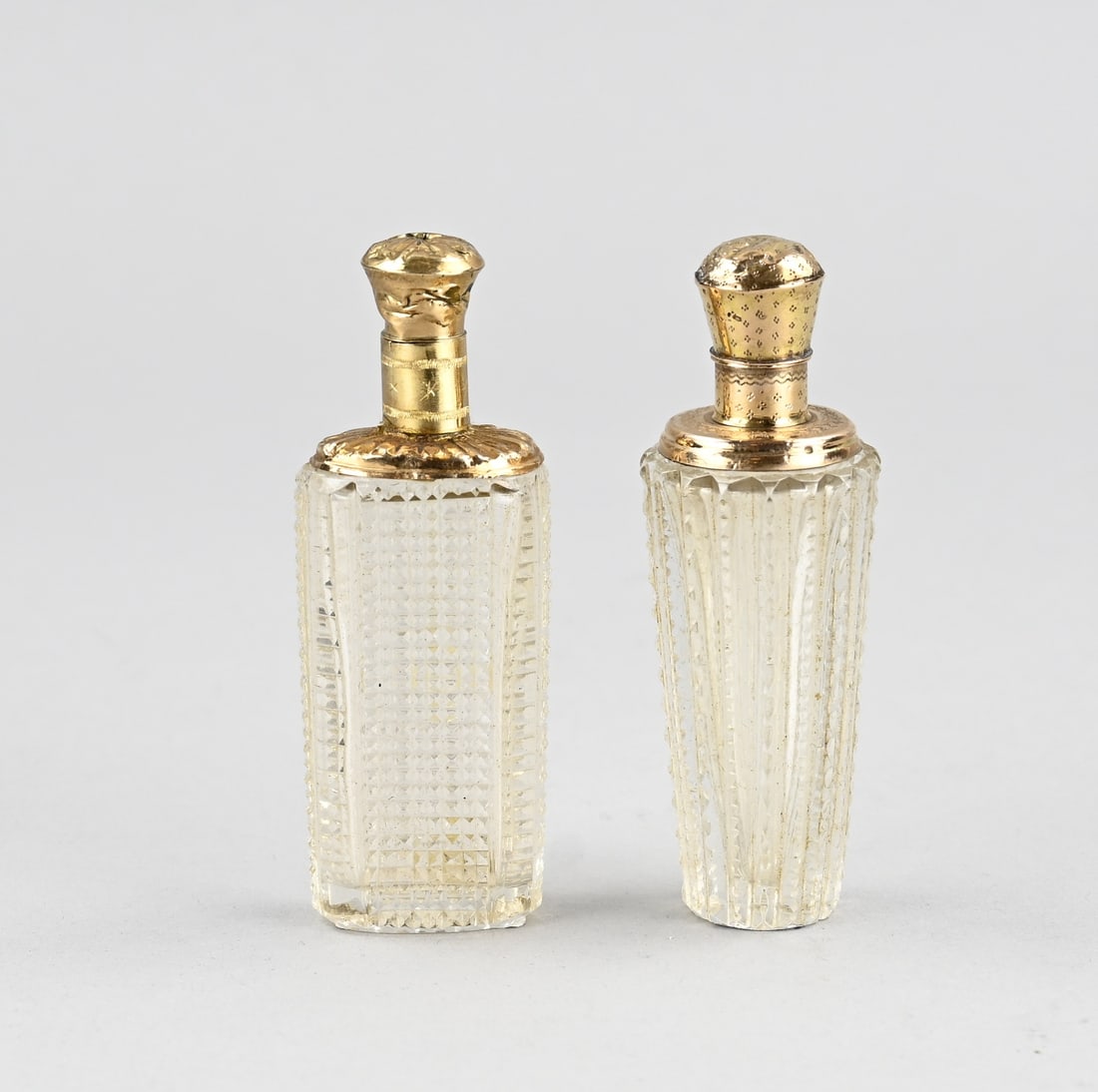 2 perfume bottles with gold: Two crystal perfume bottles with gold, 585/000. Oval-cut bottle with a wide gold collar and cap. And a conical-cut bottle with a wide gold collar and cap, hinge defective. Various dents and cracks. 9