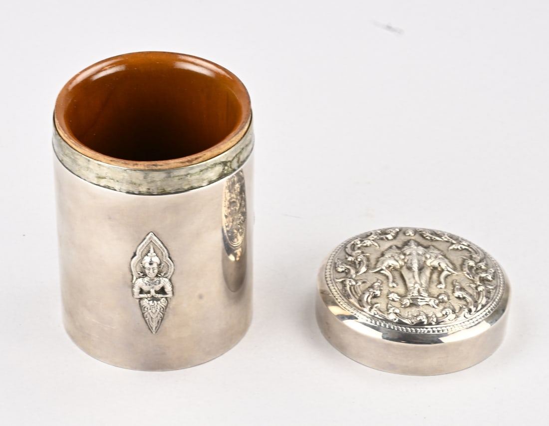 Silver lidded tin: Silver lidded box, Siam sterling 925/000, cylindrical model decorated with 3 elements featuring holy figures. The lid features hammered depictions of an erawan. The rim is engraved with: Dutch