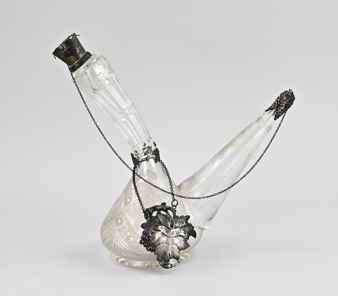Decanter with silverware: Exceptional crystal decanter with silver elements. The decanter features various cuts and 2 spouts. With stopper and cap with silver. Attached to the decanter is a leaf-shaped element, 925/000,