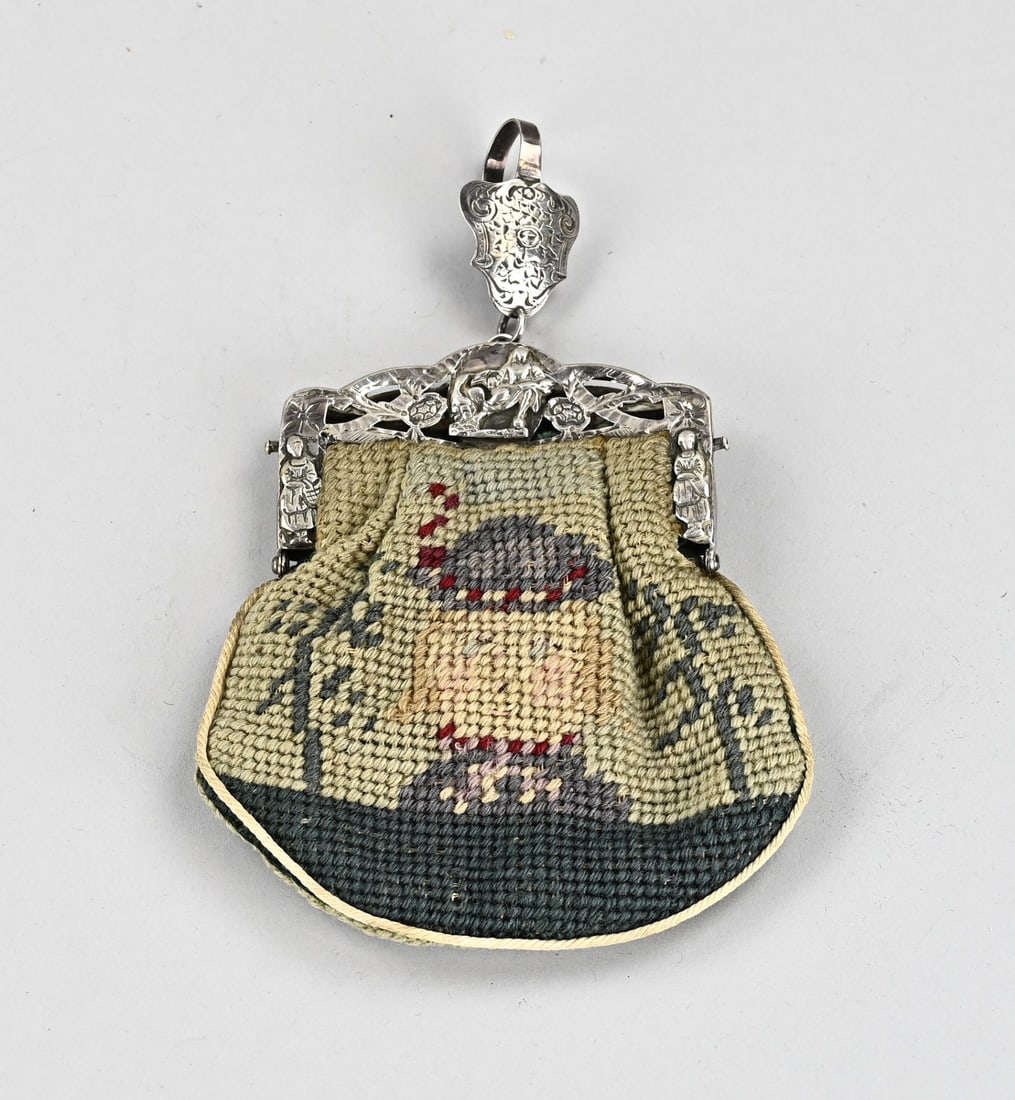 Silver children's handbag clasp & skirt hook: Small child's bag with a silver frame and skirt hook. Small rectangular contoured bag frame with sawed decoration and featuring floral decoration and figures. Attached to the frame is a contoured