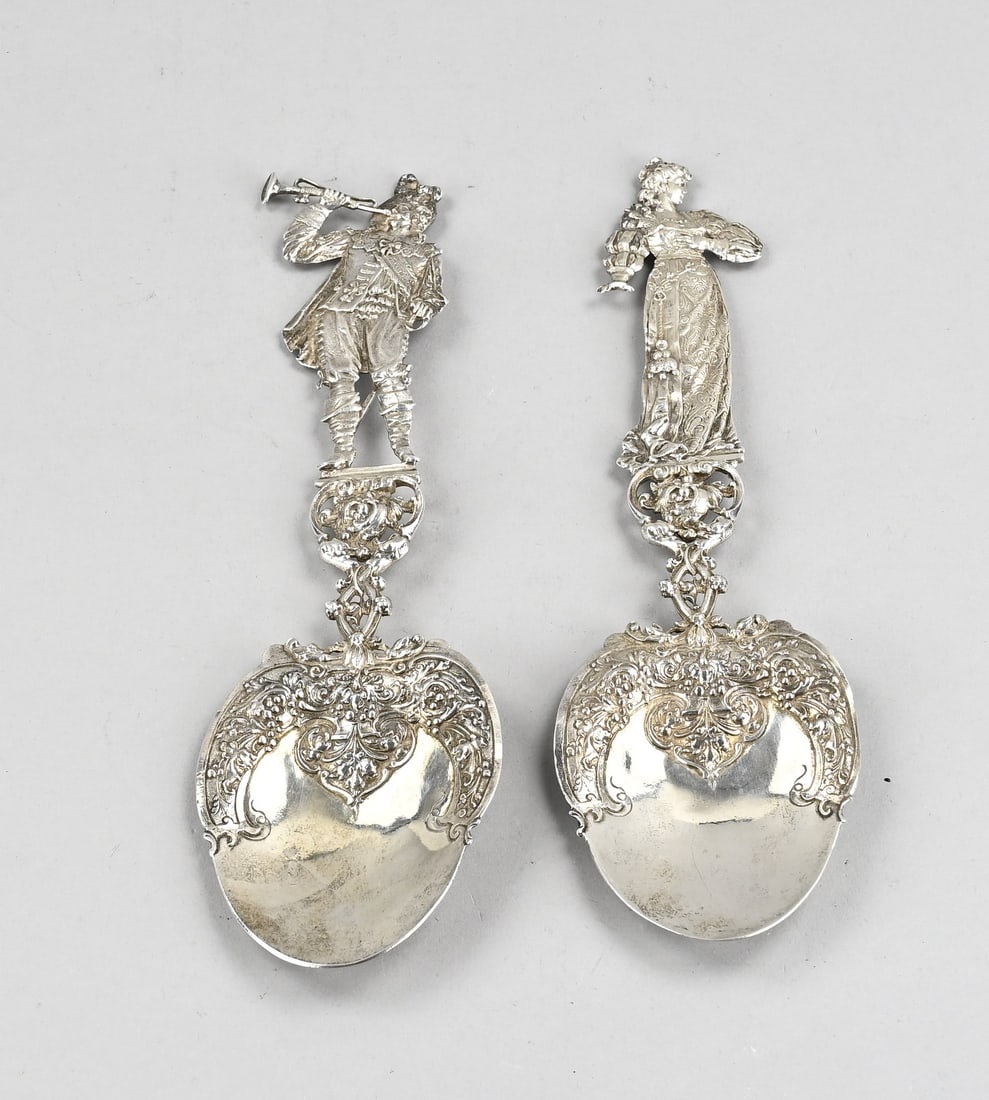 2 Silver decorative spoons: Two large silver ornamental spoons, 925/000, with a bowl with an ornate rim featuring floral decoration, attached to an ornate handle, one crowned with a man with a trumpet and the other with a noblew