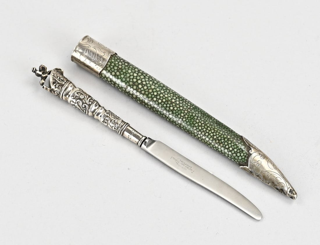 Silver travel knife in sheath: Antique travel knife in silver sheath. Knife with a silver handle decorated with floral motifs and crowned with a horseman. The knife is housed in a stingray leather sheath with silver engraving.