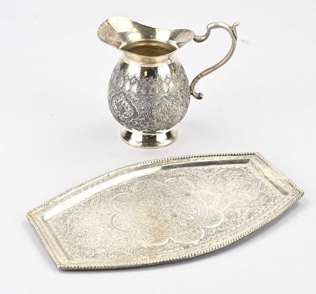 Silver tablet and milk jug, Persia: Beautiful silver tablet and milk jug, Persia, an oval contoured tablet and matching milk jug richly decorated with floral motif. 19.5x12cm and 12x6.5x10.5cm. Total approx. 316 grams. In good