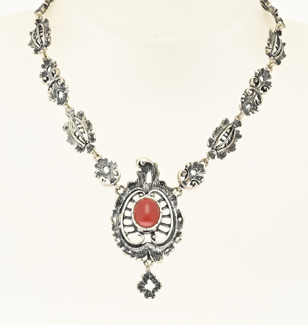 Silver choker with red coral: Silver choker, 800/000, with red coral. Choker with contoured links and a contoured openwork element with curls in the center, and an oval red coral. Length 45 cm. Width 8-48 mm. Approx. 37.6 grams.