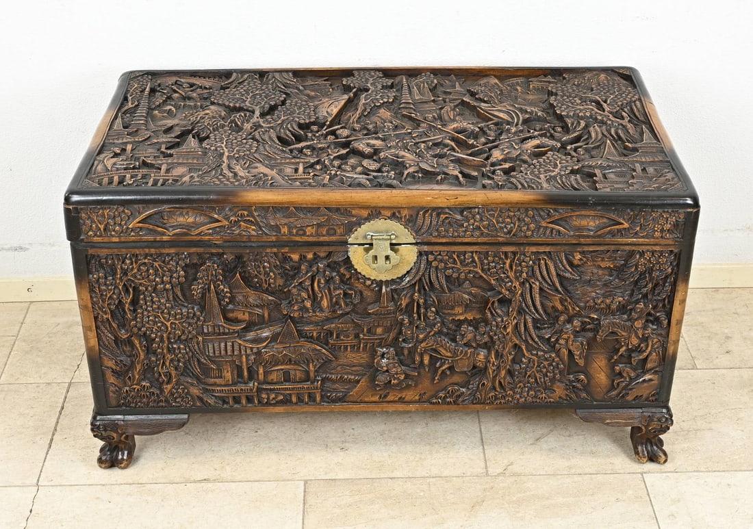 Stained Oriental camphor chest: Richly carved Oriental camphor chest with decoration of pagodas and figures in a landscape. First half of the 20th century. Dimensions: 56 x 100 x 52 cm. In good condition.