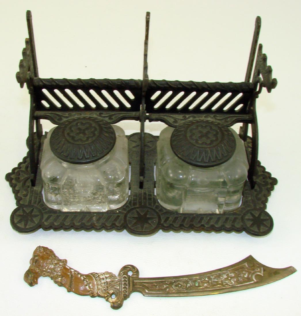 DOUBLE INKWELL PEN HOLDER with LETTER OPENER: Cast iron pen stand with letter holder, featuring two glass inkwells with hinged cast iron tops; seven pointed star motif; together with painted metal camel motif letter opener; Eastern design, tip ha