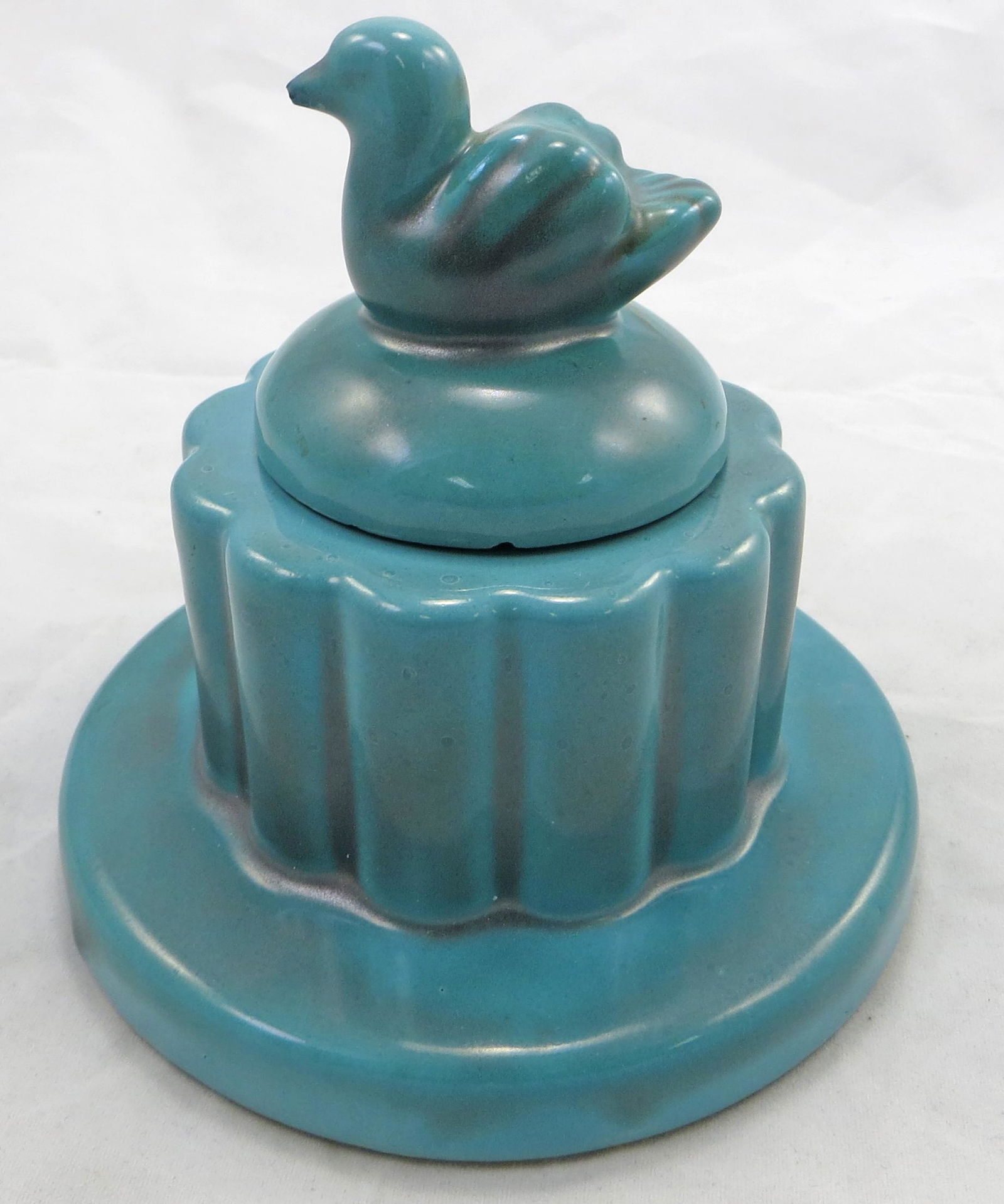 ART POTTERY INKWELL: Turquoise, Art Deco style; bird finial lid on fluted vertical ribbed bottom; yellow ware insert; bird beak has minor chip with in-painting; underside of lid has chips; mark on bottom illegible; H-4 1/