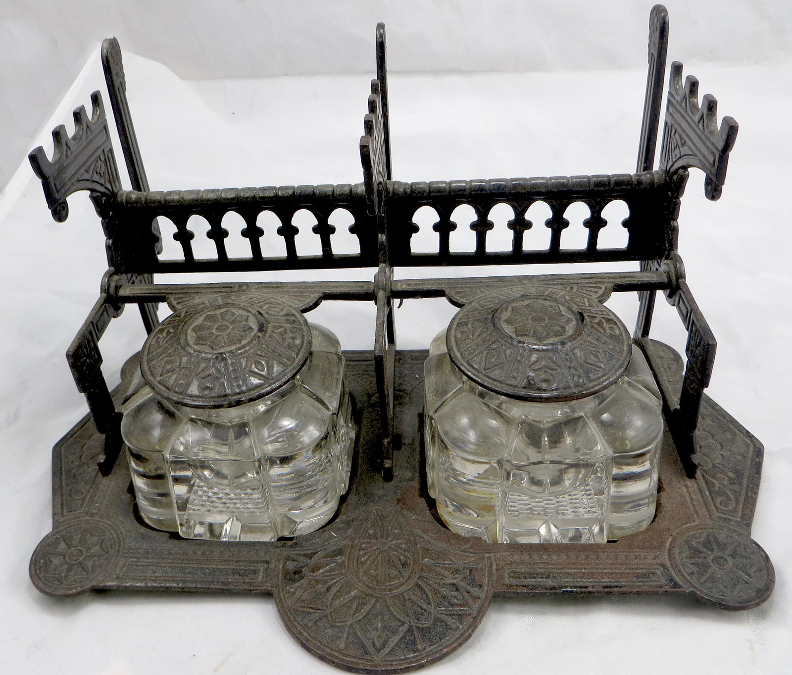 CAST IRON DOUBLE INKWELL with PEN HOLDER: Ornate cast iron inkwell/standish featuring letter holder in rear 3-slot pen holder, and double lidded inkwell, fitted for two glass lobe-form wells; some oxidation to metal, particularly to underside