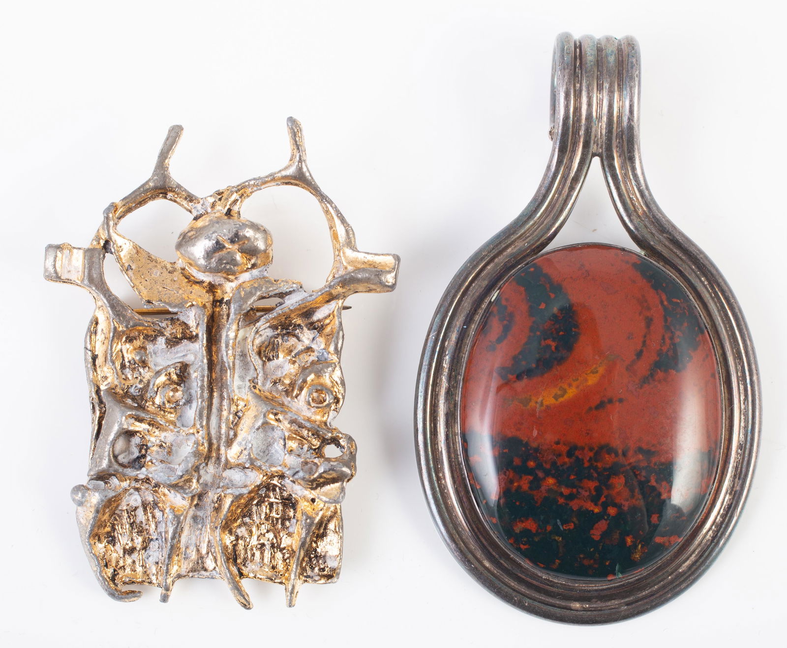 (2) MODERNIST JEWELRY PIECES: (1) large scale pendant, silvertone, large red and black jasper stone, L-3"; (1) signed Igael Tumarkin brutalist brooch, gold plated bronze, some white polish (?) residue in crevices; signed on revers