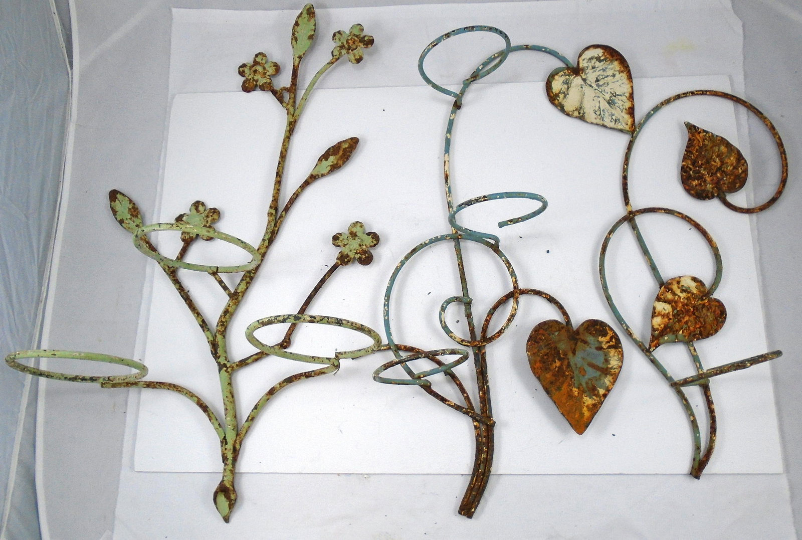 (3) METAL FLOWER POT WALL RACKS - FLORAL MOTIF: (2) matching, with leaf motif, 1-with (3) rings, 1- with (1) ring; ring Dia.-4"; (1) with flower motif, (3) rings, ring Dia.-5 1/8"; all with significant surface rust; appealing overall look, longest 