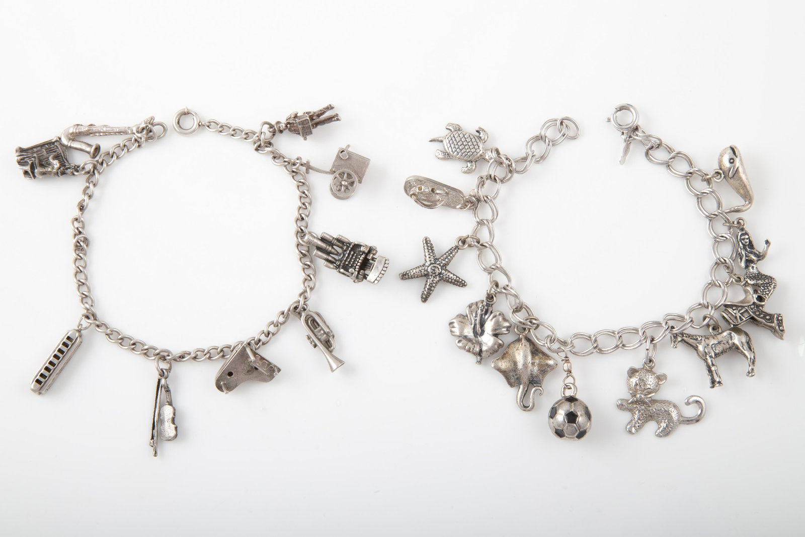 (2) VINTAGE STERLING CHARM BRACELETS: (1) music themed, including working harmonica charm, piano, violin, pipe organ, saxophone, harp, hurdy gurdy, etc., missing a charm (jump ring remains); (1) bracelet with eclectic charms: hibiscus flo