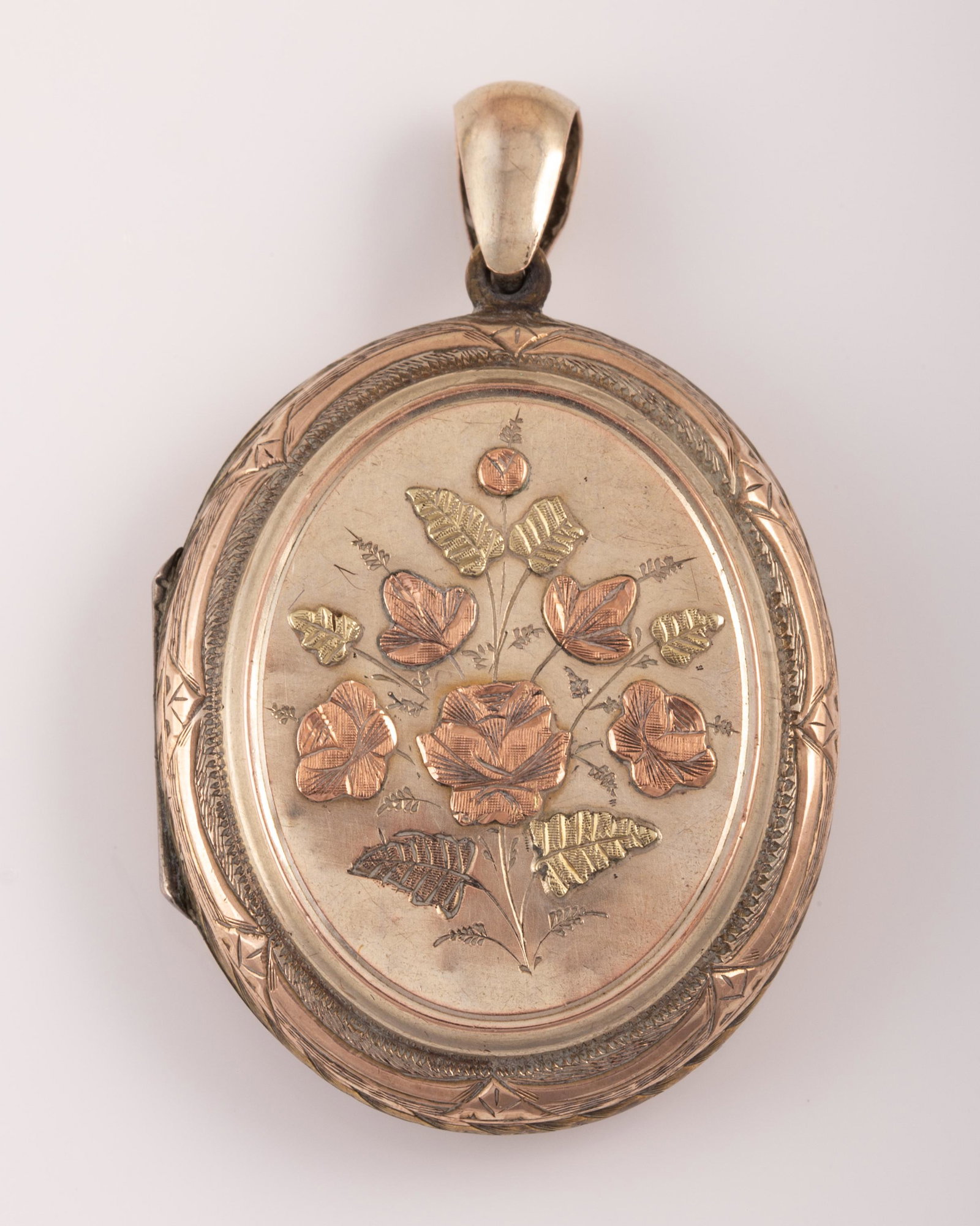 VICTORIAN GOLD TONE LOCKET with ENGRAVED FLORAL DESIGN: Elaborately engraved pale gold tone locket, featuring green and rose gold applied floral embellishments on one side, and elaborate interlacing ribbon motif on reverse, unmarked, age-appropriate wear, 