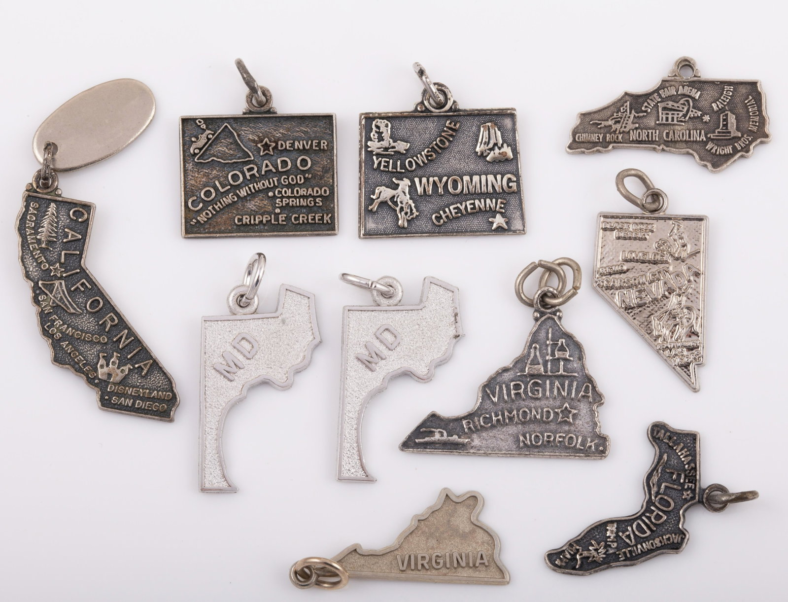 (10) STERLING SOUVENIR STATE CHARMS: 2) Maryland, 2) Virginia, 1) Florida, 1)California, 1)North Carolina, 1) Nevada, 1) Wyoming, 1) Colorado. .59 ozt., (1) missing jump ring. L - 1" G - VG