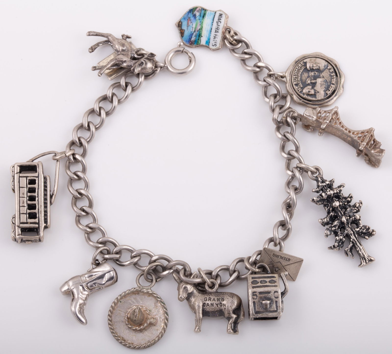STERLING CHARM BRACELET: 11 Charms: cowboy boot, sombrero, slot machine, pine tree, bridge, trolley, Arizona, Virginia, etc.; 1. ozt L - 6 3/4" G - VG