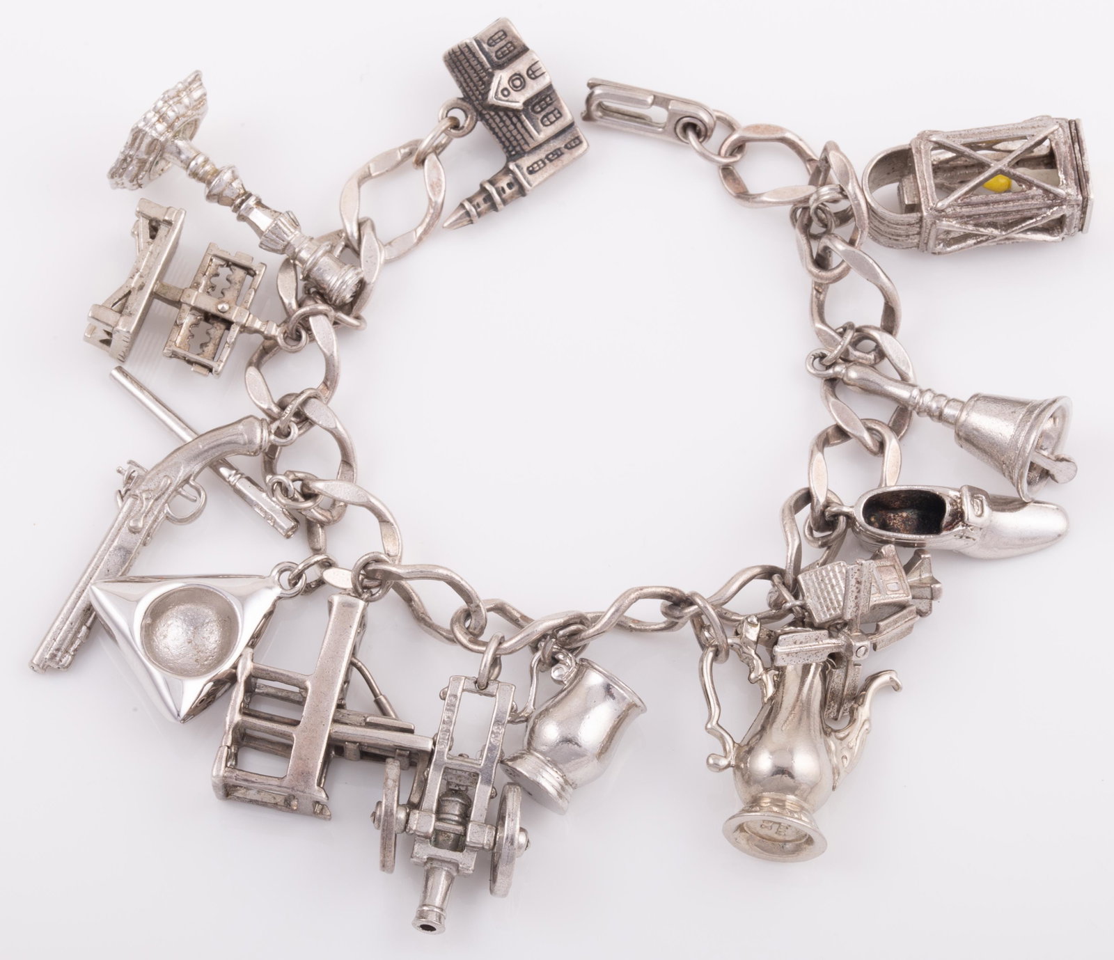 STERLING CHARM BRACELET: 14 Charms: lantern, bell. teapot, stein, windmill, tricorne, revolver, candlestick, shoe, canon, etc.; 2.58 ozt L - 7 1/2" G - VG