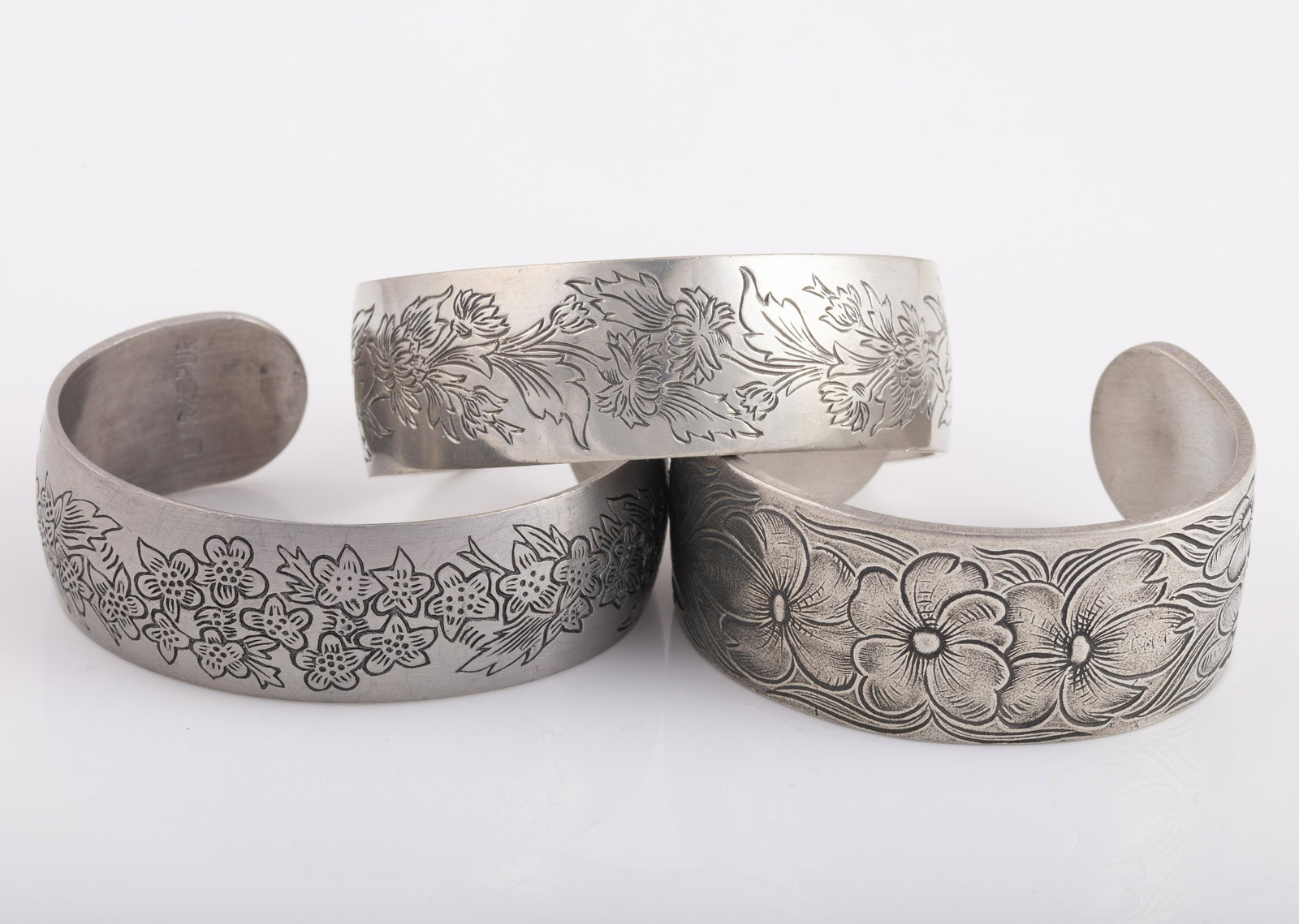 (3) PEWTER CUFF BRACELETS: LEONARD, KIRK STIEFF & SALISBURY: Each cuff features an etched floral design: (1) Salisbury Pewter, dogwood pattern; (1) Leonard Pewter with Larkspur design; (1) Kirk Stieff with Chrysanthemum design; L-6 3/4"-7", EX