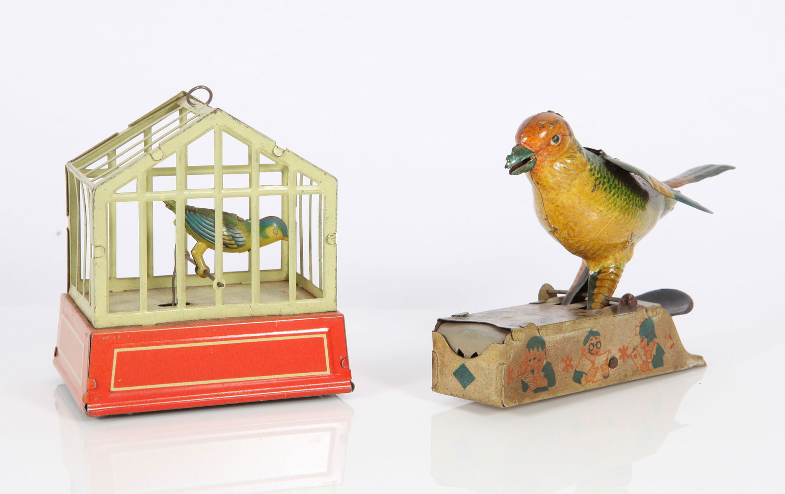 (2) VINTAGE GERMAN MECHANICAL BIRD TOYS: Tin litho; (1) U. S. Zone Germany; bird in cage; key-wind; bird moves up and down and tweets; (1) Germany, clicker toy, bird's head goes down and is supposed to grab a tiny fotune envelope in his beak