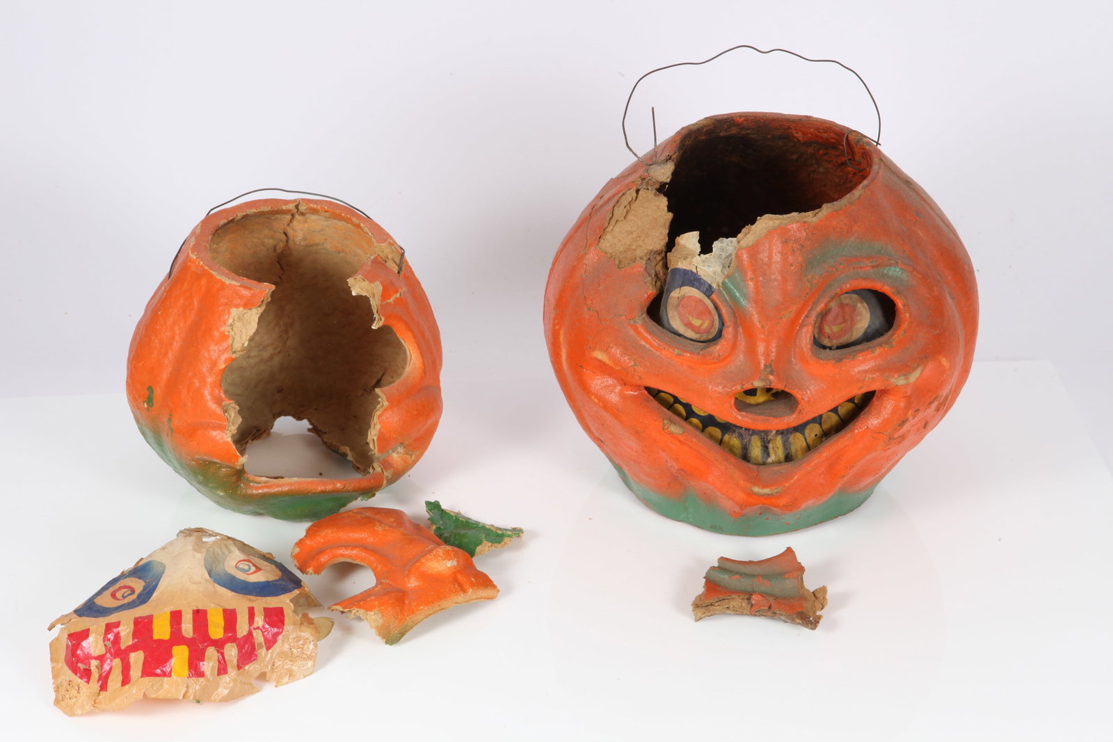 (2) VINTAGE HALLOWEEN JACK-O-LANTERNS: Painted papier mache, printed paper inserts; wire handles; selling as is, both in need of restoration; large jack o'lantern has large tear over left eye and rim; melted wax in bottom; medium jack o'la