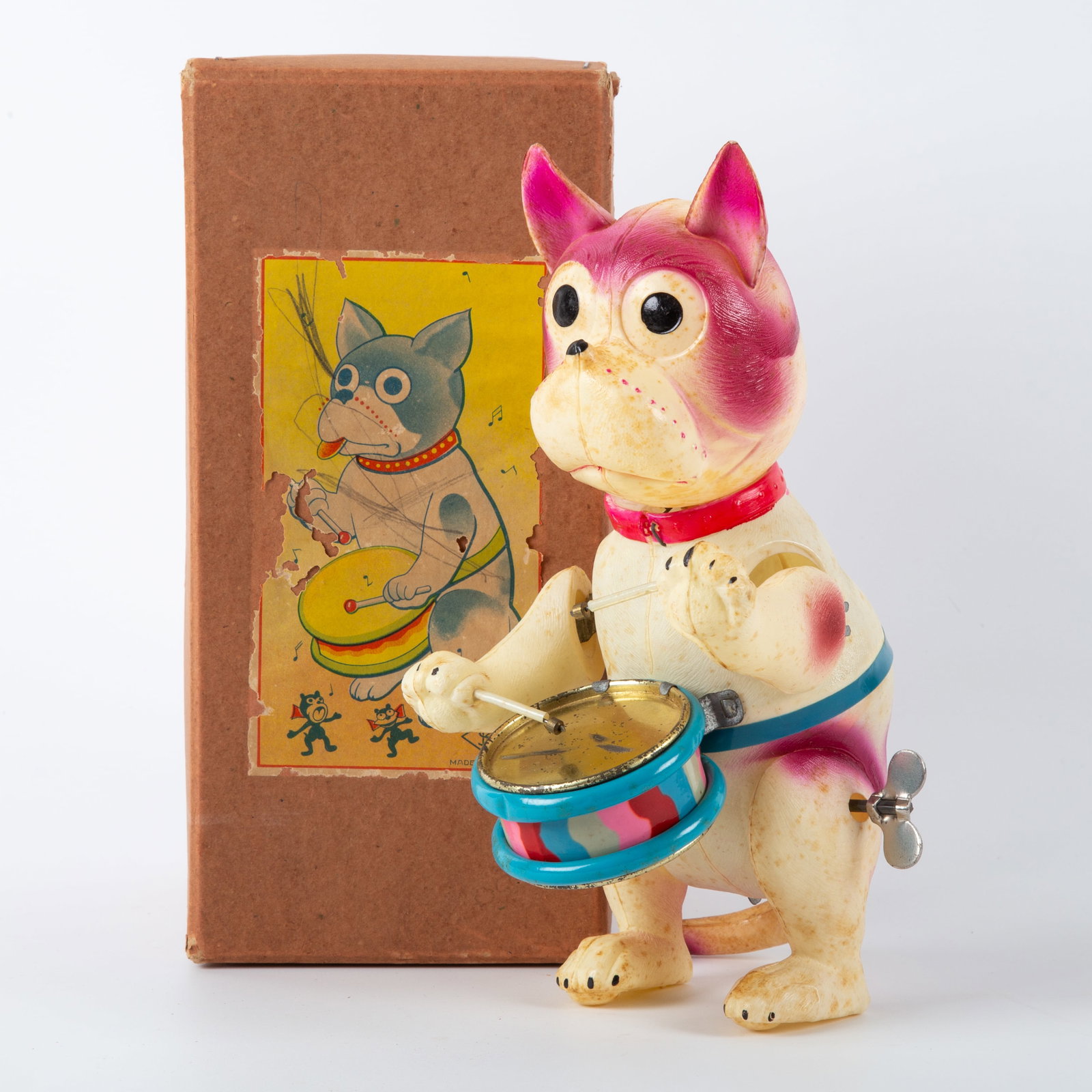 DRUMMING BONZO DOG CELLULOID with ORIGINAL BOX: Celluloid clockwork drumming dog; wind-up mechanism works; doggie drums and moves head from side to side; marked Made in Japan; box marked " Made in Japan"; original cardstock box has graphic paper l