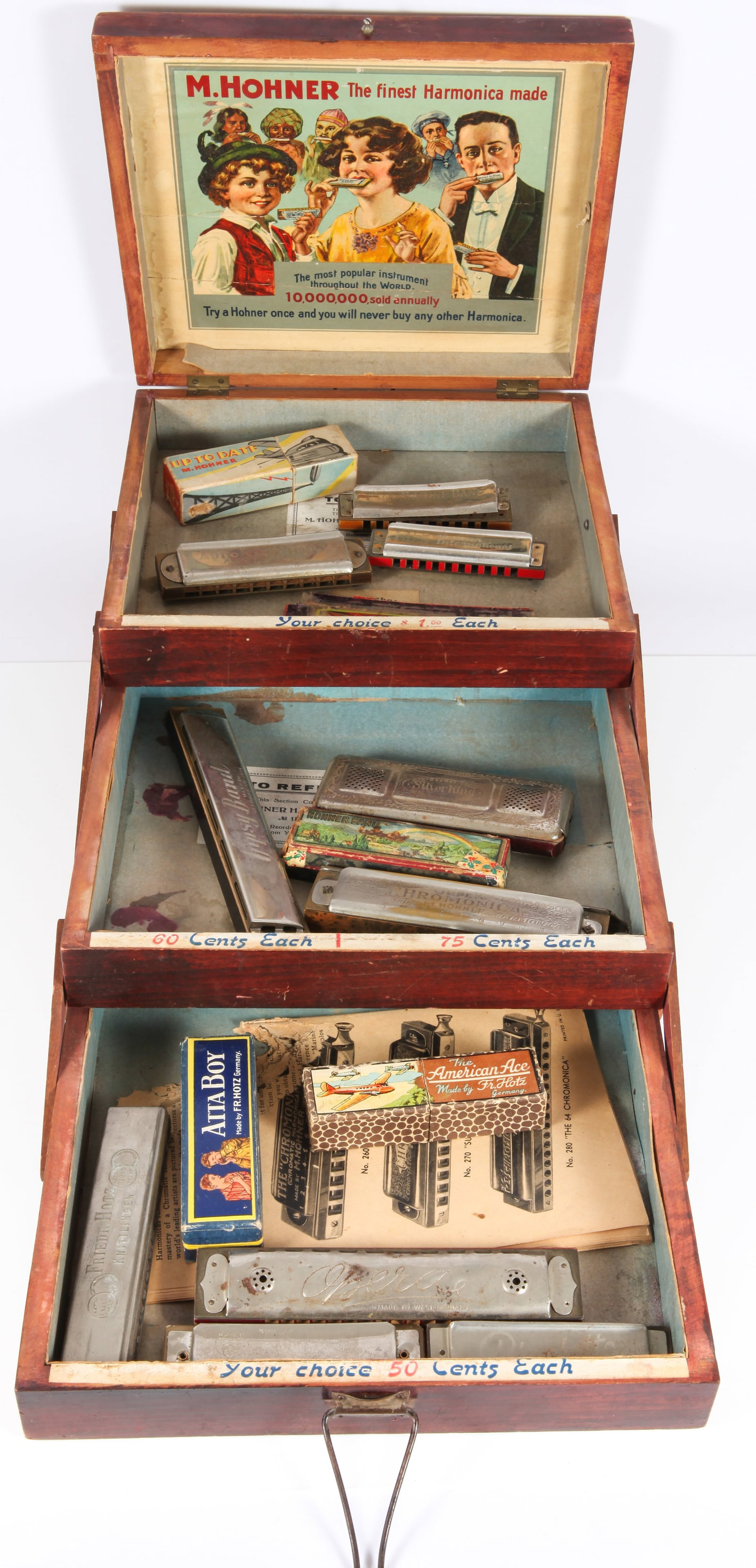 M. HOHNER HARMONICA ADVERTISING BOX with HARMONICAS: Three tiered telescoping box: wood, stenciled top, paper litho advertisement on interior of lid; " Your Choice 50 cents, 60 cents, 75 cents and 1 dollar"; (13) assorted harmonicas, mostly German; (6) 