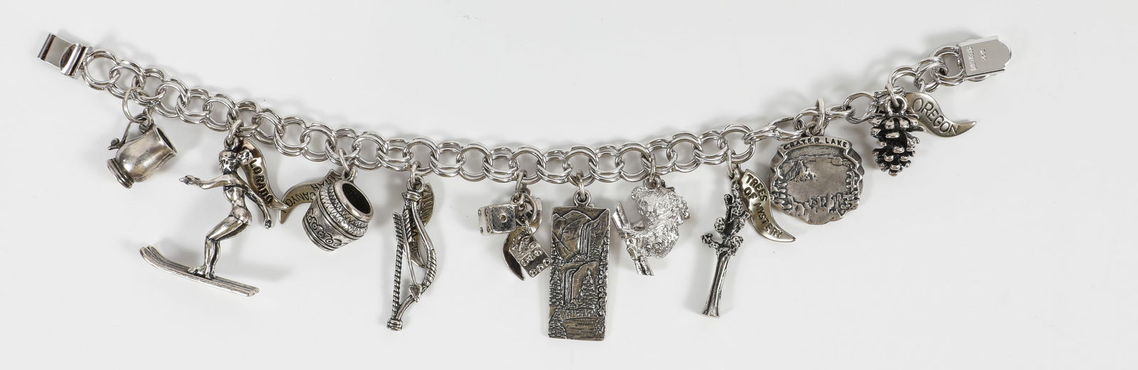 STERLING CHARM BRACELET: (16) charms: (6) flags: Oregon, Trees of Mystery, Yosemite National Park, Bryce Canyon Utah, Colorado; stein, skier, pot, bow and arrow, dice, Yosemite Falls, koala bear, tree, Crater Lake, pinecone;
