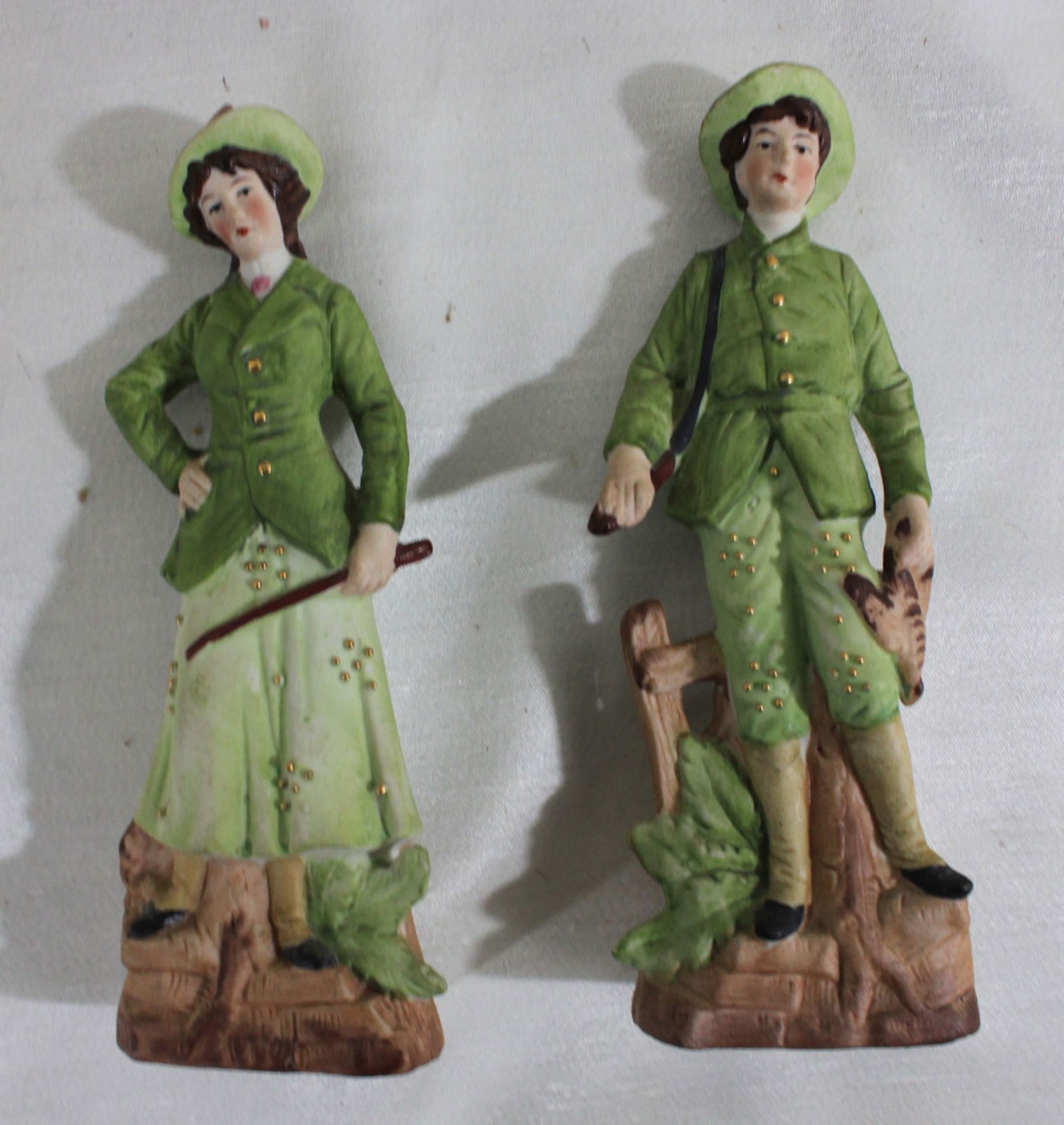 Pair of German Bisque Porcelain Figurines, Hunters: Pair of German Bisque Porcelain Figurines, Hunters Charming pair of early 20th-century German bisque porcelain figurines, each depicting a young gentleman and lady in matching green hunting attire. Th