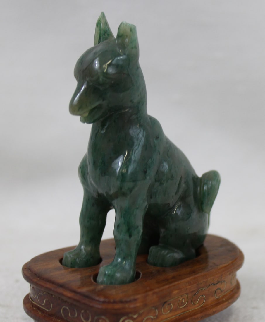 Chinese Carved Jade Figure of a Dog on Stand: Chinese Carved Jade Figure of a Dog on Stand Well-carved jade figure of a seated dog with upright ears and curled tail, rendered in a mottled green stone with natural variations. Presented on a fitted