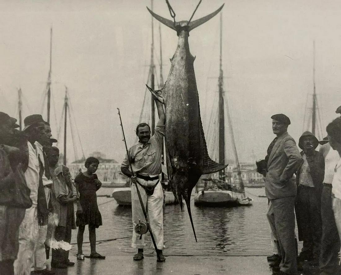 Ernest Hemingway - Ernest Standing Next to a Blue Marlin: ERNEST HEMINGWAY (1899-1961) Ernest standing next to a 420 pound, 12 foot long Blue Marlin. Print in Colors 6 1/2" x 8" Ernest Hemingway, in full Ernest Miller Hemingway, (born July 21, 1899, Cicero [