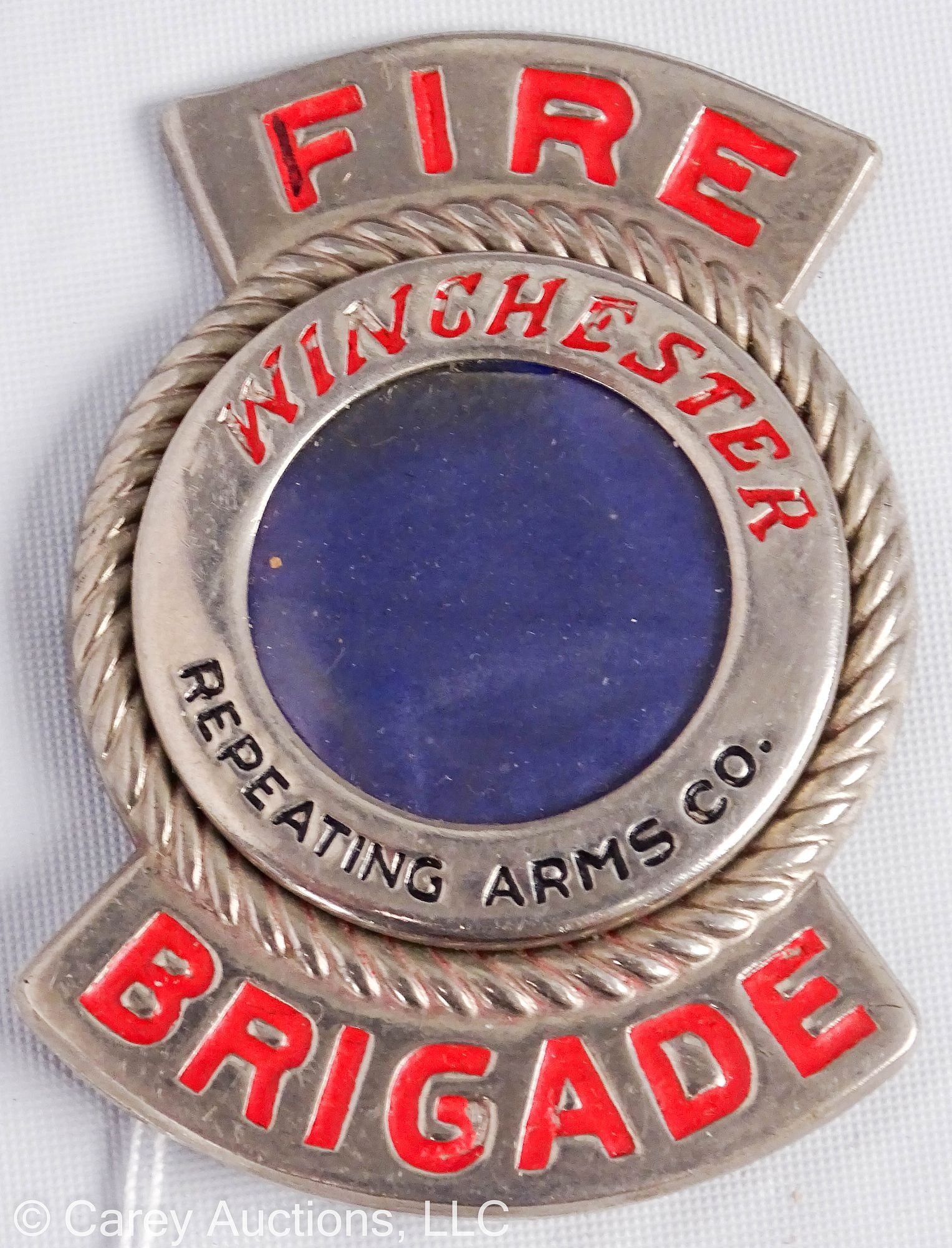 WINCHESTER REPEATING ARMS CO FIRE BRIGAGE BADGE/PIN: A pressed steel Fire Brigade badge/pin from the Winchester Repeating Arms Co. private fire department. Blue fabric encased behind a plastic window, red and black enamel in the recessed lettering. Mark