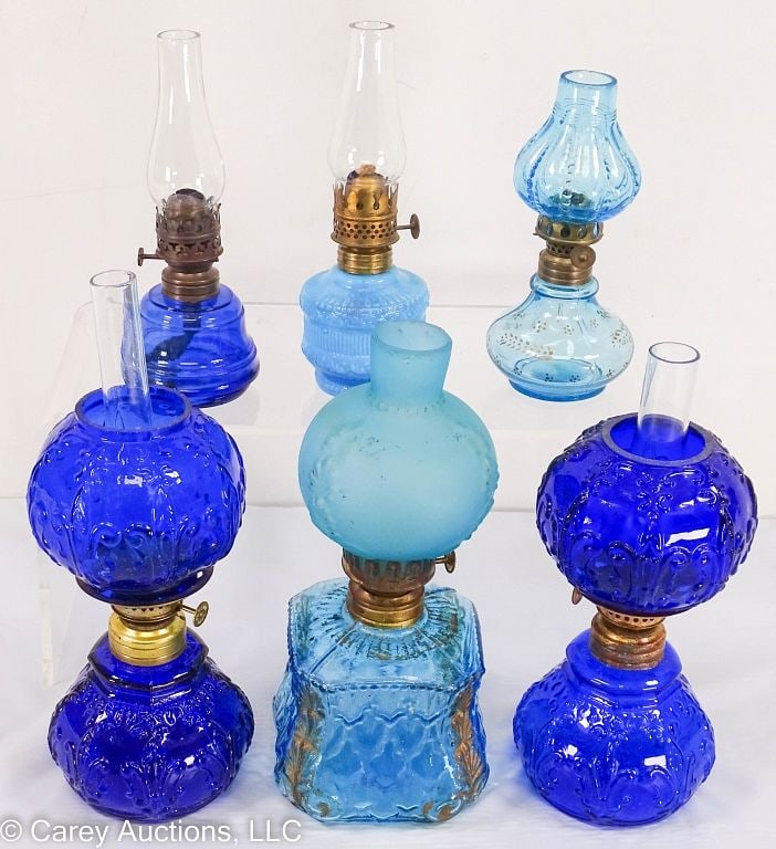 6 BLUE GLASS MINIATURE OIL LAMPS incl NORTHWOOD: Cobalt blue pair, marked with Northwood [N] with nutmeg burners / Large transparent blue lamp may not have the original shade. / Measures: 6.5"H to 9.5"H / Condition: All lamps in good condi