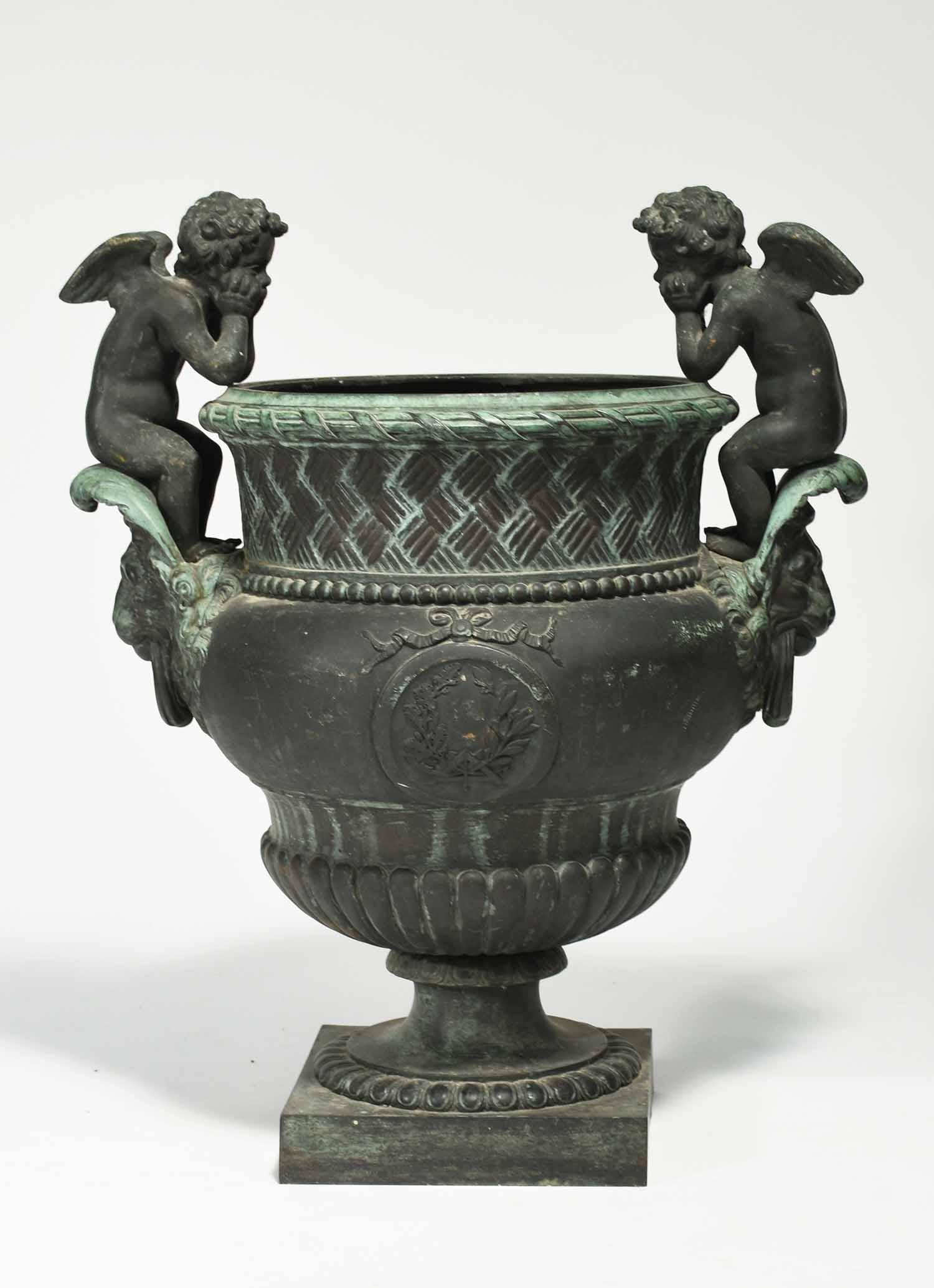 19th C. European bronze urn: 19th C. European bronze urn with lions head handles topped with contemplative putti, basket weave keck with gadrooned base and foot. 24”H x 22”W x 13” dia. of urn
