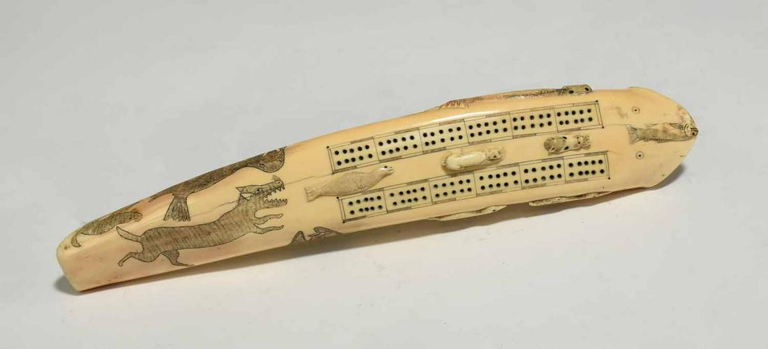 Inuit Carved Walrus Tusk Cribbage Board: Northwest coast/Inuit carved walrus tusk cribbage board inscribed with walruses, seal, fishermen. Also with relief carving of birds, seals, fish. 14.5”L x 2.5”W. 2 lbs.